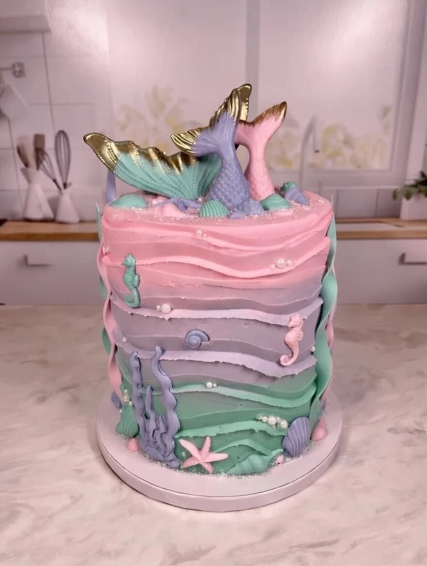 Pastel mermaid cake with pink, purple, and mint wave layers, gold-tipped mermaid tails, seahorses, and pearl accents