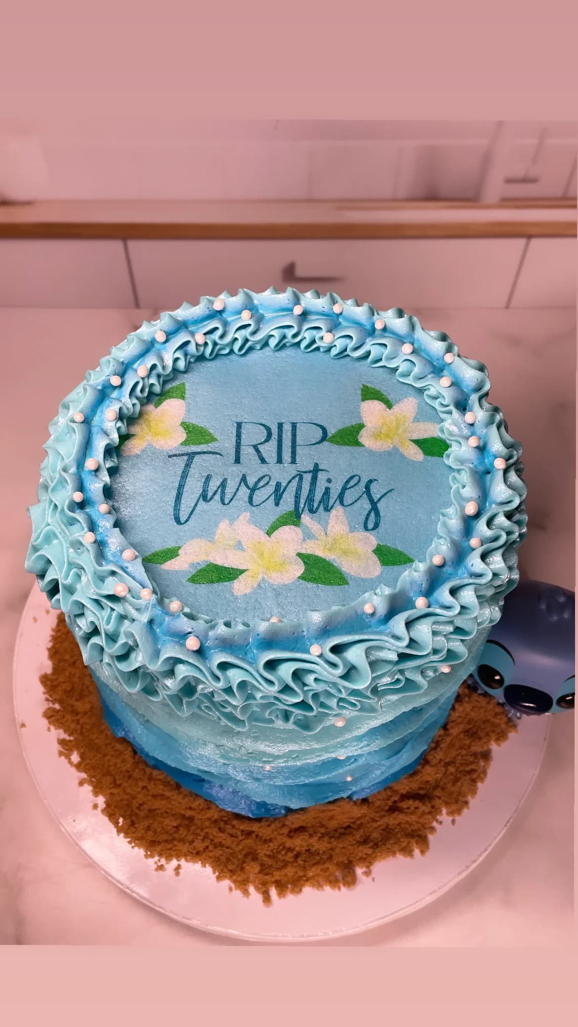 Blue ocean themed RIP Twenties 30th birthday cake with ruffled waves, sandy beach base, and floral topper