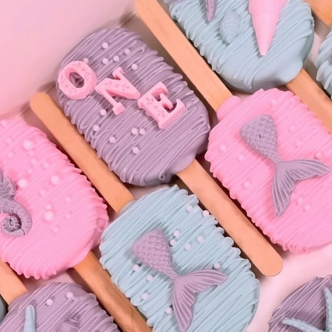 Decorated mermaid-themed cakesicles in pink, purple, and blue